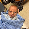 Tatum is registered to the contest to win money with this photo: baby, infant, child, portrait, face, eyes, looking_at_camera, blanket, blue_blanket, swaddled, newborn, indoor, stroller, toy_vehicle, yellow, wheel, floor, adult_hand, cozy, photography