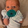 baby, infant, child, portrait, pacifier, blue_pacifier, bib, checkered_bib, blue_clothing, lying_down, indoors, bed, pillow, close_up, face, eyes, wide_eyed, baby_clothing, cozy, photograph