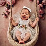 baby, infant, smiling, happy, swing, knitted_swing, white_dress, bow_headband, floral_embroidery, pink_roses, flowers, flower_background, cute, portrait, child, indoor, decor, soft_lighting, innocence, joy
