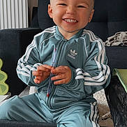 Alessio participe au concours pour gagner de l'argent avec cette photo : adidas, casual, child, clothing, couch, cute, face, furniture, happy, home, indoor, living_room, pen, person, portrait, sitting, smiling, toddler, toy, tracksuit