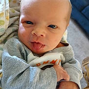 Robert is registered to the contest to win money with this photo: baby, infant, face, tongue_out, blanket, clothing, hand, cozy, indoor, carpet, couch, polka_dot, cute, expression, newborn, portrait, child, person, soft_light, closeup