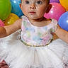 Amelia is registered to the contest to win money with this photo: baby, child, tutu, dress, balloons, colorful, curious, sitting, portrait, celebration, party, cute, infant, face, eyes, hands, feet, indoors, soft_lighting, happy