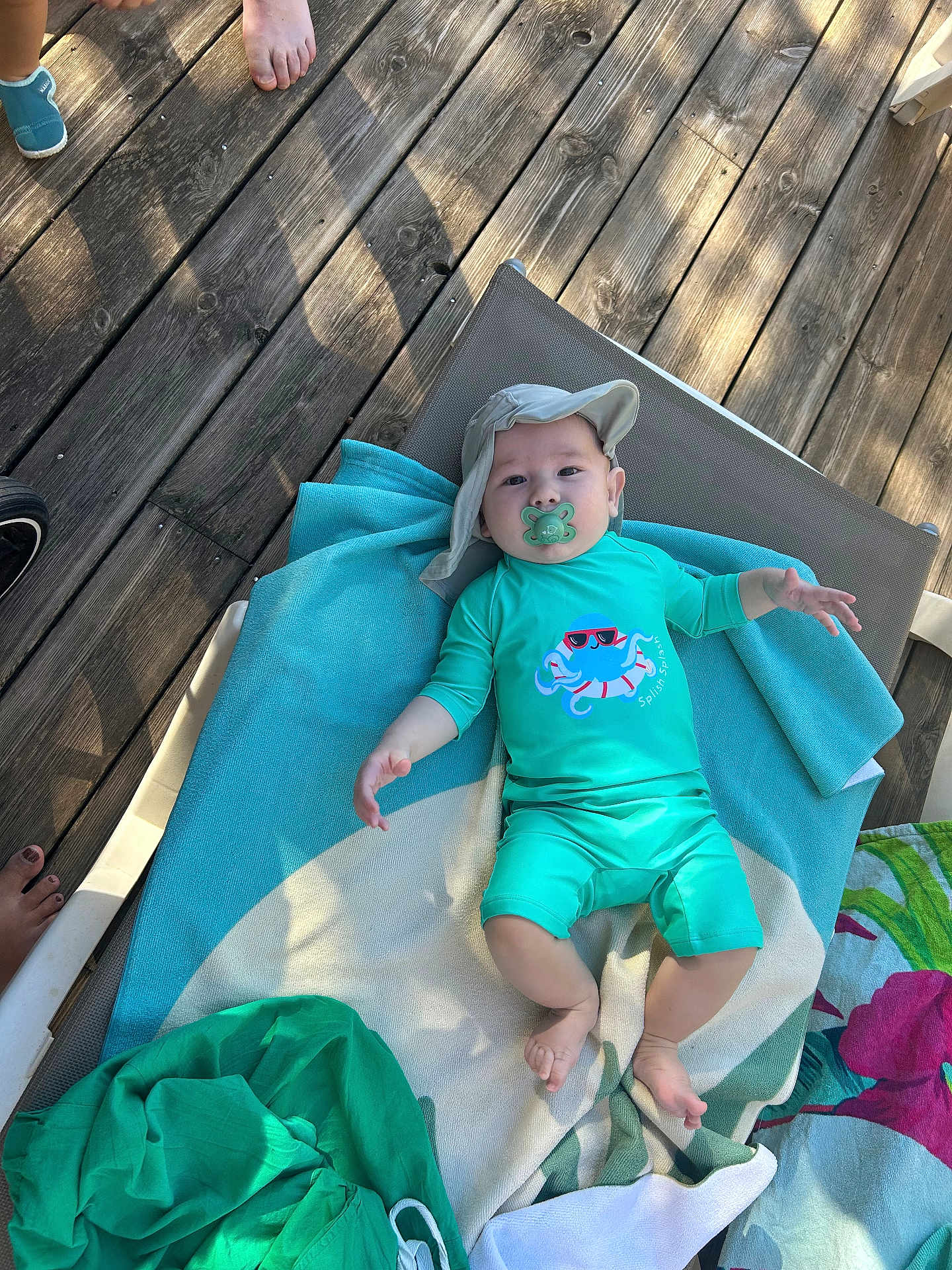 Tiziano participe au concours pour gagner de l'argent avec cette photo : baby, pacifier, hat, towel, sunbed, wooden_floor, feet, outdoor, clothing, child, relaxing, turquoise, babywear, summer, shade, person, infant, flooring, resting, cute
