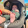 baby, blue_sky, car_seat, child, clothing, fabric, fence, foot, green_pants, hand, infant, outdoor, pacifier, patio, person, pool, seat_belt, stroller, sunlight, tree