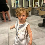 Lynéo participe au concours pour gagner de l'argent avec cette photo : toddler, child, striped_clothing, romper, hair, face, indoor, salon, floor, tile, person, blurred_background, furniture, mirror, chair, standing, curious, modern, casual_clothing, young