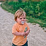 Benji is registered to the contest to win money with this photo: toddler, child, pacifier, orange_tshirt, black_shoes, shorts, walking, gravel_path, outdoor, greenery, trees, overcast_sky, nature, serious_expression, young_child, casual_clothing, daylight, dirt_road, cute, small_person
