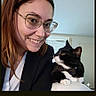 woman, cat, tuxedo_cat, smiling, glasses, portrait, indoor, selfie, black_and_white_cat, bow_tie, pet, person, face, hair, clothing, window, couch, home, photography, animal