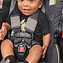 baby, car_seat, smiling, child, infant, safety_harness, black_clothing, socks, happy, person, seat, indoor, cute, toddler, face, hand, grinning, young_child, clothing, seatbelt