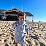 Amante is registered to the contest to win money with this photo: child, toddler, beach, sand, curly_hair, barefoot, tracksuit, blue_sky, outdoor, sunny, building, pavilion, walking, person, clothing, daytime, cute, serious_expression, nature, recreation