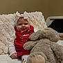 baby, bow, red_clothing, plush_toy, bunny, blanket, smiling, indoors, child, cute, soft_texture, cozy, sitting, person, headband, toy, happy, infant, warm, comfort