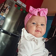 Vyctoire a rejoint le concours — aidez-le/la à gagner de superbes lots ! baby, child, pink_bow, headband, white_clothing, indoor, kitchen, fridge, red_wall, person, cute, portrait, holding, blue_eyes, infant, smile, toddler, cozy, home, face