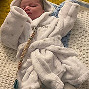 Archie joined the competition — help win amazing prizes! baby, sleeping, white_robe, booties, blanket, knitted_blanket, pacifier_clip, indoor, cozy, child, infant, soft, cute, peaceful, sleep, yellow_background, textured_background, clothing, person, resting