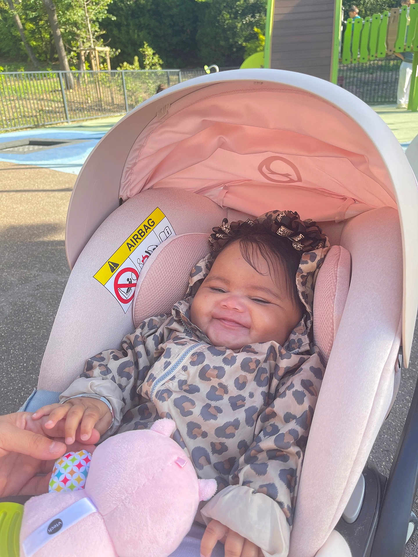 Mélina a rejoint le concours — aidez-le/la à gagner de superbes lots ! baby, car_seat, leopard_print, jacket, toy, pink, smiling, child, outdoor, playground, sunlight, hand, person, infant, cute, seat, hood, comfort, happy, young