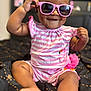baby, child, sunglasses, pink, striped_clothing, dimples, smiling, sitting, barefoot, indoors, romper, cute, portrait, young_child, happy, fashion, accessory, black_blanket, pattern, closeup