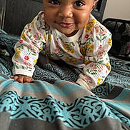 Heaven is registered to the contest to win money with this photo: baby, child, crawling, smiling, face, eyes, sweater, floral_pattern, bed, blanket, blue, gray, hand, indoors, cute, person, portrait, cozy, happy, young