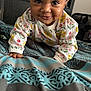 baby, child, crawling, smiling, face, eyes, sweater, floral_pattern, bed, blanket, blue, gray, hand, indoors, cute, person, portrait, cozy, happy, young