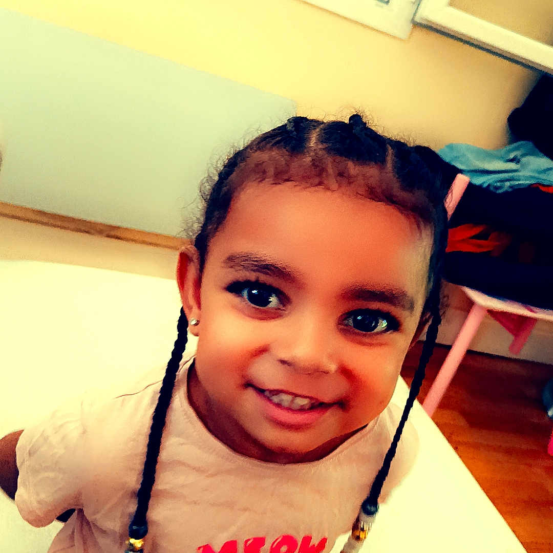 Djasmine a rejoint le concours — aidez-le/la à gagner de superbes lots ! beads, braids, casual, cat_graphic, child, clothing, cute, earrings, floor, furniture, happy, home, indoor, person, portrait, room, smiling, tshirt, window, young_child