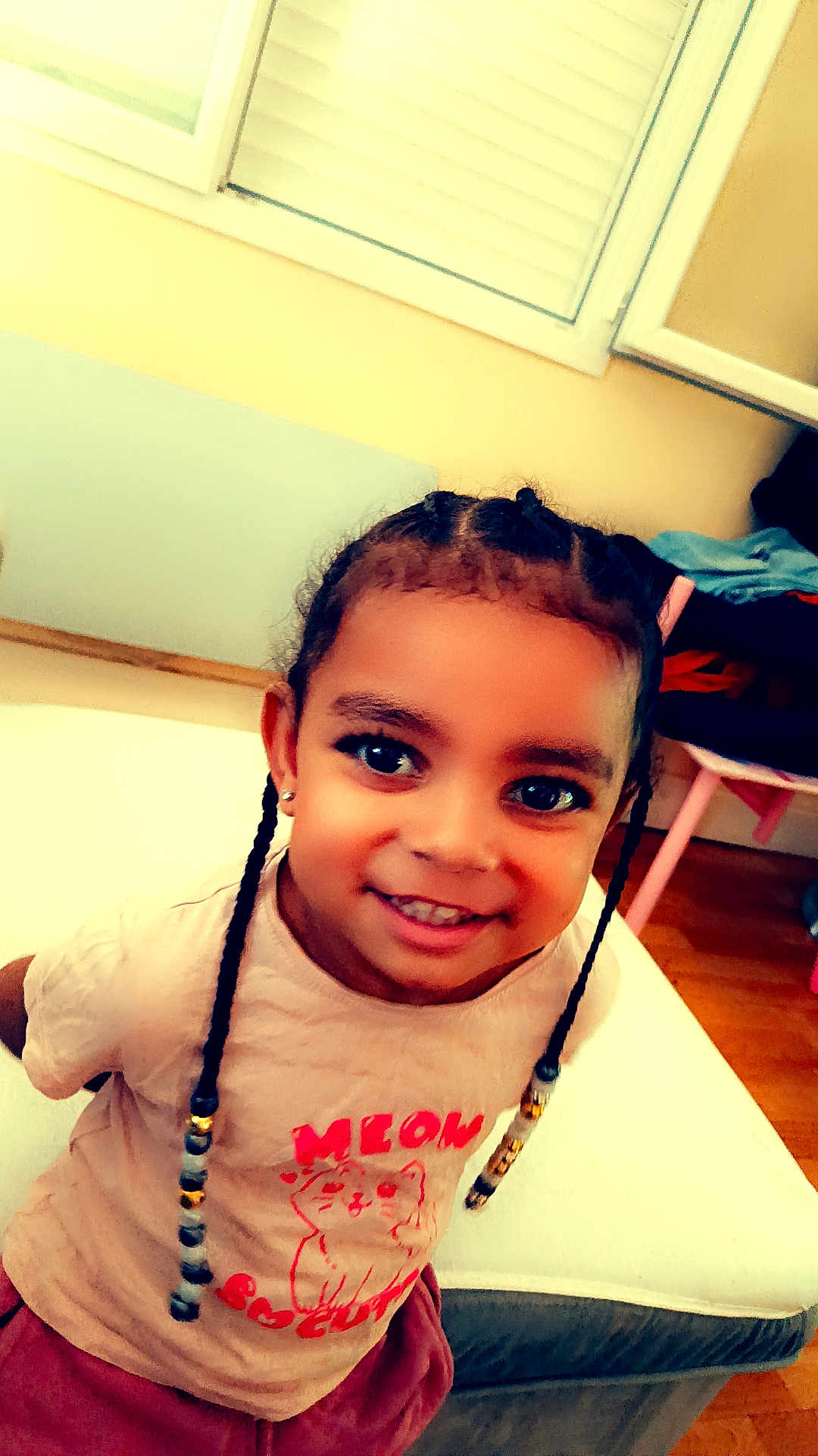 Djasmine a rejoint le concours — aidez-le/la à gagner de superbes lots ! beads, braids, casual, cat_graphic, child, clothing, cute, earrings, floor, furniture, happy, home, indoor, person, portrait, room, smiling, tshirt, window, young_child