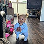 toddler, child, indoor, living_room, wooden_floor, clapping, happy, smiling, pigtails, white_clothing, toy, pink_toy, television, furniture, window, daylight, flooring, person, home, casual