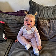 Scarlet-Rose is registered to the contest to win money with this photo: baby, child, pigtails, smile, pink_outfit, white_socks, couch, pillows, indoor, happy, cute, portrait, seated, blonde_hair, young_child, home, cozy, textured_fabric, small_person, casual