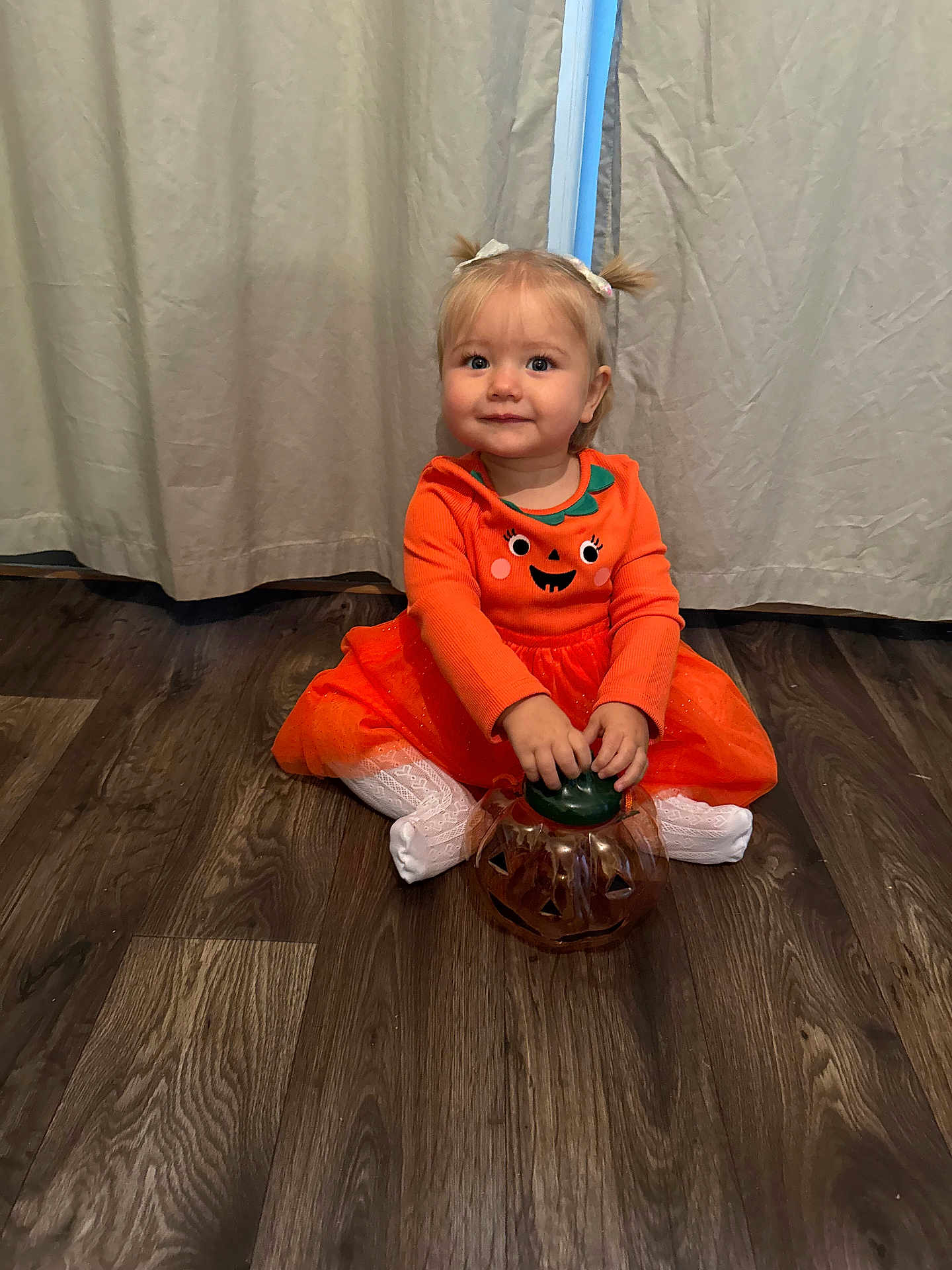 Scarlet-Rose is registered to the contest to win money with this photo: child, toddler, pumpkin, orange_dress, white_tights, plastic_container, floor, wood_floor, curtains, indoor, smiling, baby, pigtails, hair_bows, festive, halloween, cute, sitting, portrait, person