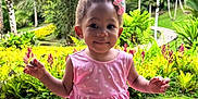 Kehlany a rejoint le concours — aidez-le/la à gagner de superbes lots ! toddler, child, pink_dress, flower_hair_clip, bench, wooden_bench, sandals, greenery, tropical_plants, flowers, outdoor, nature, smiling, portrait, cute, garden, grass, trees, sunlight, happy