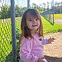 child, girl, smiling, outdoor, daylight, fence, bench, grass, field, nature, headband, long_hair, casual_clothing, happy, portrait, person, sunlight, park, playground, cute