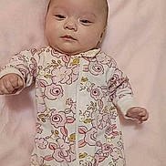 Leah is registered to the contest to win money with this photo: baby, infant, onesie, floral_pattern, blanket, pink, face, child, newborn, lying_down, soft_texture, cute, person, sleepwear, toddler, indoors, portrait, skin, head, hand