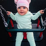 Leanna is registered to the contest to win money with this photo: baby, child, swing, playground, hat, pom_poms, clothing, chains, seat, smiling, happy, outdoor, person, infant, blue_socks, pastel_colors, cute, seated, fun, play