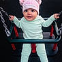 baby, child, swing, playground, hat, pom_poms, clothing, chains, seat, smiling, happy, outdoor, person, infant, blue_socks, pastel_colors, cute, seated, fun, play