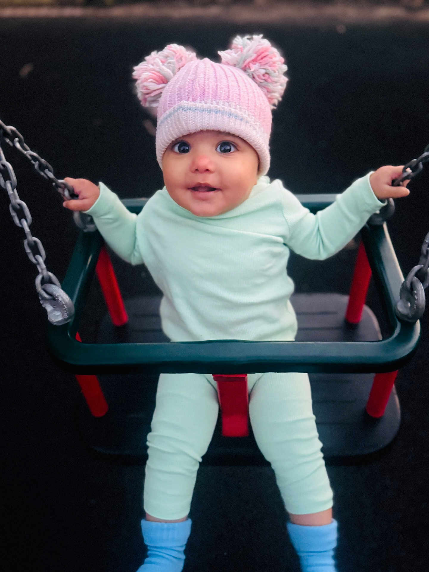 Leanna is registered to the contest to win money with this photo: baby, child, swing, playground, hat, pom_poms, clothing, chains, seat, smiling, happy, outdoor, person, infant, blue_socks, pastel_colors, cute, seated, fun, play