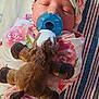 baby, pacifier, plush_toy, headband, bow, blanket, floral_pattern, sleeping, child, infant, striped_surface, pink, blue, soft_toy, cute, resting, indoors, closeup, wrapped, peaceful