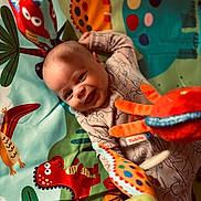 Atlas is registered to the contest to win money with this photo: baby, smiling, play_mat, dinosaur, plush_toys, colorful, infant, happy, child, cute, indoors, toy, playtime, fabric, pattern, crawling, clothing, head, face, cheerful