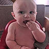 baby, child, high_chair, indoor, curious, chewing, fingers, skin, arm, face, wide_eyes, window, natural_light, wooden_sign, background, person, seated, red, cozy, home
