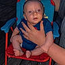 Buckley is registered to the contest to win money with this photo: baby, child, infant, red_eye, chair, hands, person, outdoor, wooden_deck, night, clothing, blue_shirt, red_chair, support, sitting, footwear_absent, close_up, portrait, human, adult_hand