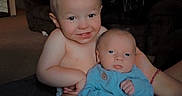 Buckley is registered to the contest to win money with this photo: baby, brother, child, clothing, cousin, cute, expression, family, head, holding, indoor, infant, living_room, person, sitting, skin, smiling, sofa, toddler, young