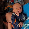Buckley joined the competition — help win amazing prizes! baby, infant, onesie, dinosaur_pattern, person, hand, arm, toy_box, toys, blue_shirt, indoor, smile, face, newborn, cuddling, child, cute, holding, cozy, playful