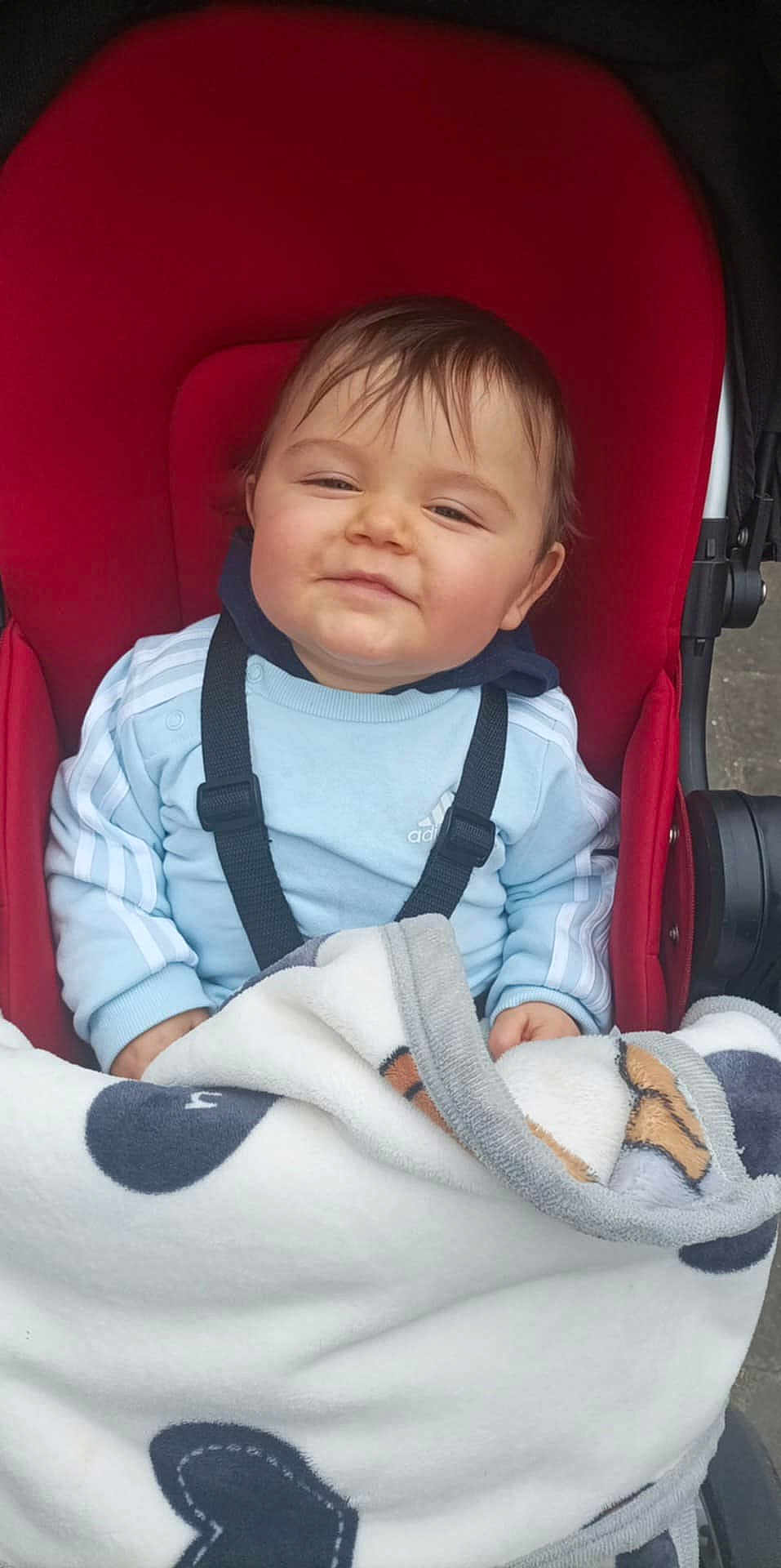 Hugo participe au concours pour gagner de l'argent avec cette photo : baby, child, stroller, blanket, red, blue_sweatshirt, smile, face, person, clothing, outdoor, happy, hoodie, baby_seat, cozy, infant, cute, bundle, casual, comfort