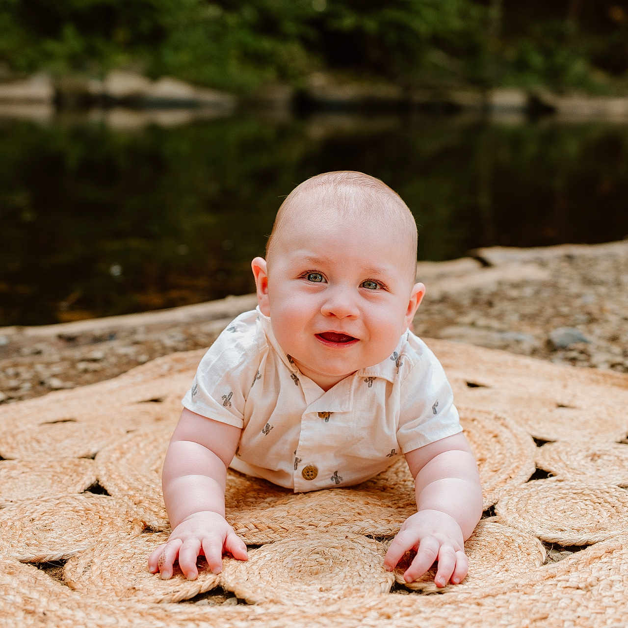Oliver is registered to the contest to win money with this photo: baby, child, crawling, cute, face, grass, greenery, hands, infant, mat, nature, outdoor, pebbles, portrait, relaxing, river, shirt, smiling, summer, woven_mat
