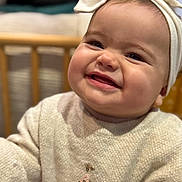 Alba a rejoint le concours — aidez-le/la à gagner de superbes lots ! baby, child, smiling, face, headband, sweater, indoors, portrait, happy, cute, infant, closeup, cozy, warm_lighting, wooden_crib, clothing, seated, expression, toddler, headwear
