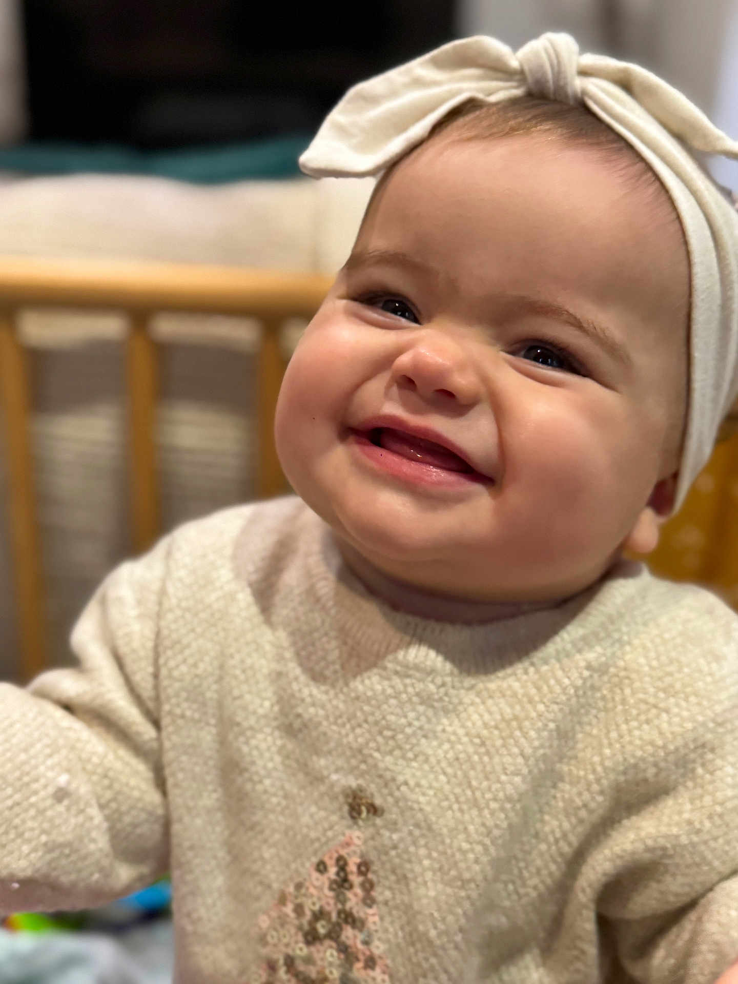 Alba a rejoint le concours — aidez-le/la à gagner de superbes lots ! baby, child, smiling, face, headband, sweater, indoors, portrait, happy, cute, infant, closeup, cozy, warm_lighting, wooden_crib, clothing, seated, expression, toddler, headwear
