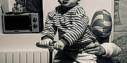 Rafael participe au concours pour gagner de l'argent avec cette photo : toddler, child, toy_car, vintage_toy, striped_shirt, hand, balloon, party, celebration, indoors, radiator, microwave, table, confetti, sock, curious, support, furniture, monochrome, portrait