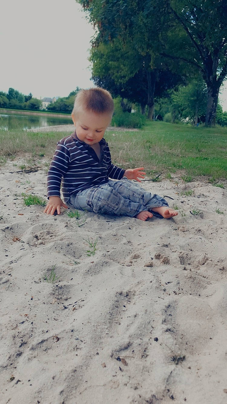 Marwann participe au concours pour gagner de l'argent avec cette photo : baby, baby_toddler_clothing, barefoot, fun, grass, happy, landscape, leisure, people_in_nature, person, plant, play, recreation, sand, shirt, sitting, sky, soil, t_shirt, toddler