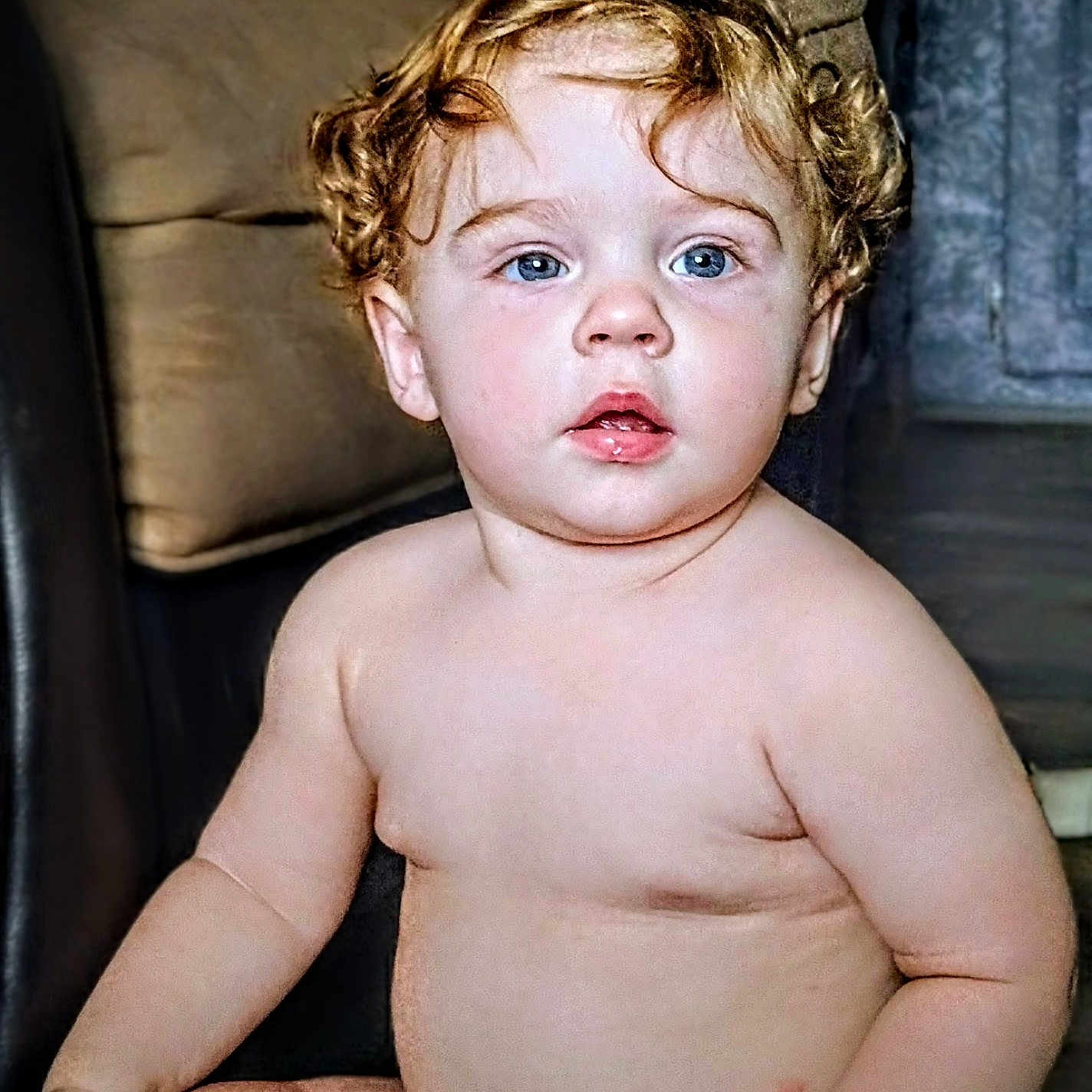 Braxton is registered to the contest to win money with this photo: baby, child, toddler, curly_hair, blue_eyes, skin, indoor, couch, furniture, sitting, diaper, innocent, portrait, cute, chubby, face, person, young, curious, soft_lighting