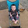 baby, stroller, child, outdoor, concrete, blue_stroller, pet_food_bowl, baby_clothing, baby_face, baby_feet, welcome_mat, gravel, wheel, seat_belt, casual_wear, infant, expression, person, daylight, sidewalk