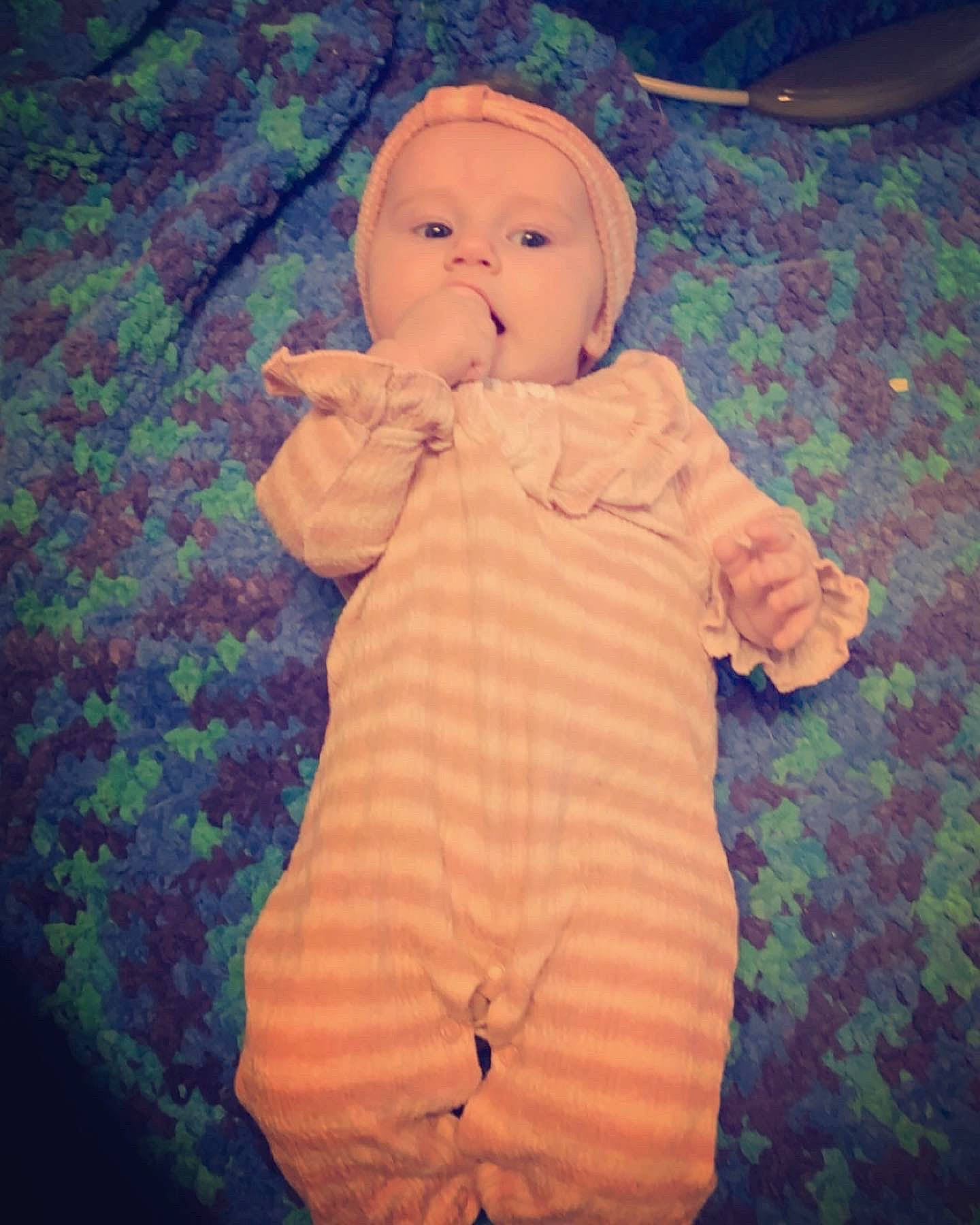 Stella is registered to the contest to win money with this photo: arm, baby, baby_toddler_clothing, cheek, cloud, doll, face, gesture, hand, happy, head, headwear, human_body, nose, orange, organ, person, pink, skin, sleeve