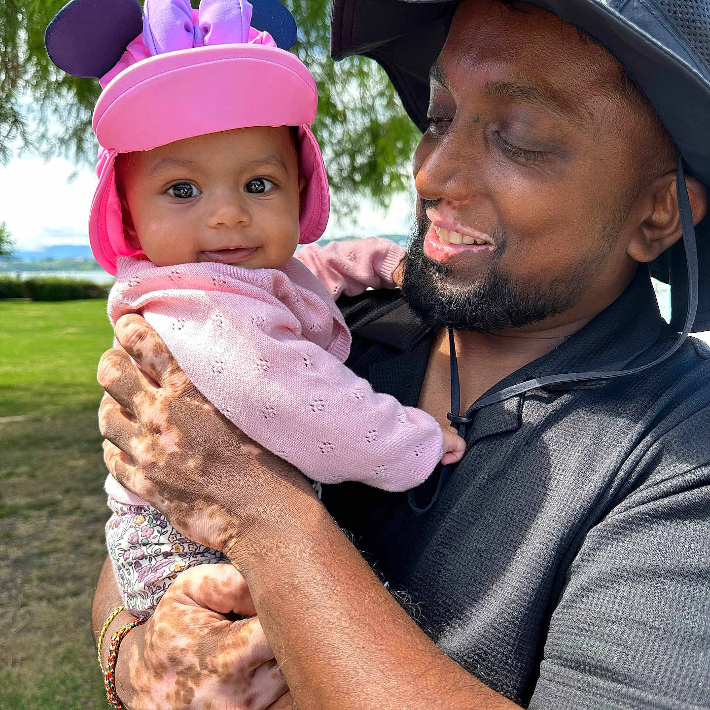 Ysanah participe au concours pour gagner de l'argent avec cette photo : affection, baby, casual_clothing, child, daylight, family, grass, greenery, happy, hat, holding, man, nature, outdoor, pink_hat, portrait, purple_bow, smile, sunlight, tree