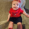 Bena is registered to the contest to win money with this photo: american_flag, baby, blanket, celebration, child, cute, face, furniture, happy, headband, indoor, infant, patterned_socks, portrait, red_clothing, seated, shorts, smile, socks, soft_texture