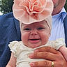Bena is registered to the contest to win money with this photo: adult_hand, baby, blue_suit, child, clothing, cute, daylight, flower_headband, greenery, happy, headwear, holding, infant, nature, outdoor, person, portrait, ring, skin, smile