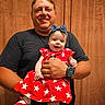 man, baby, child, smile, red_dress, headband, watch, curtain, portrait, indoor, happy, holding, star_pattern, casual_clothing, family, human, people, person, father, infant